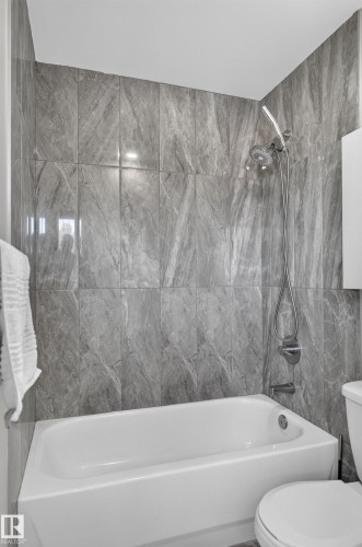 White bathtub with a chrome showerhead and gray tile surround - 8632 184 Street Nw, Edmonton, AB - Indoor Photo Showing Bathroom
