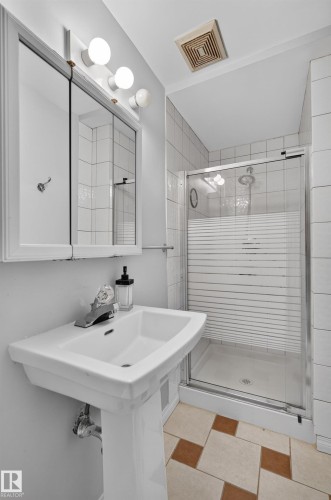 Pedestal sink with chrome faucet, mirrored medicine cabinet with integrated lighting, glass-enclosed shower with white tiled walls, and patterned floor tile - 8632 184 Street Nw, Edmonton, AB - Indoor Photo Showing Bathroom