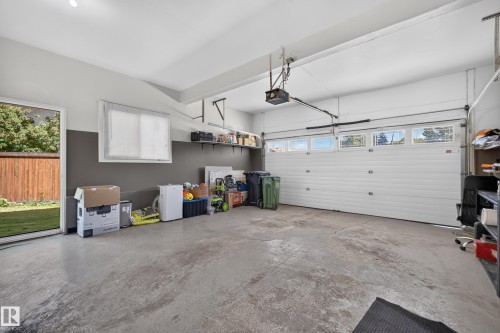 Attached garage with a roll-up door featuring upper window panels, a side entry door, and a built-in shelving system - 8632 184 Street Nw, Edmonton, AB - Indoor Photo Showing Garage