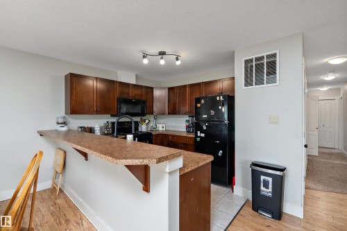 Kitchen featuring wood-finish cabinetry, solid surface countertops, a built-in microwave, and a black appliance package - 203 Graybriar Green, Stony Plain, AB - Indoor Photo Showing Kitchen With Double Sink