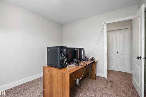 Textured carpet flooring, neutral wall paint, white trim, and white bi-fold closet doors - 203 Graybriar Green, Stony Plain, AB - Indoor Photo Showing Office