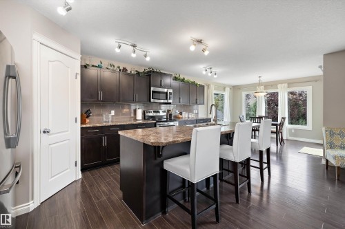 Open-concept kitchen with wood-finish flooring, dark wood cabinetry, stainless steel appliances, and a central island with an extended countertop - 3922 Agar Court Sw, Edmonton, AB - Indoor Photo Showing Other Room