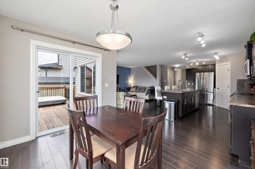 Open-concept layout featuring wood-finish flooring, a dining area, and a kitchen with dark cabinetry, stainless steel appliances, and a central island - 3922 Agar Court Sw, Edmonton, AB - Indoor Photo Showing Other Room