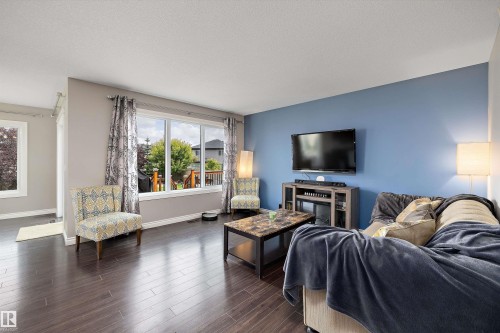 Dark wood-finish flooring complemented by a vibrant accent wall - 3922 Agar Court Sw, Edmonton, AB - Indoor Photo Showing Living Room