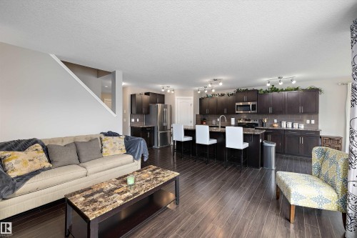 Hardwood-finish flooring throughout, dark wood cabinetry, stainless steel appliances, and a kitchen island with seating - 3922 Agar Court Sw, Edmonton, AB - Indoor Photo Showing Living Room