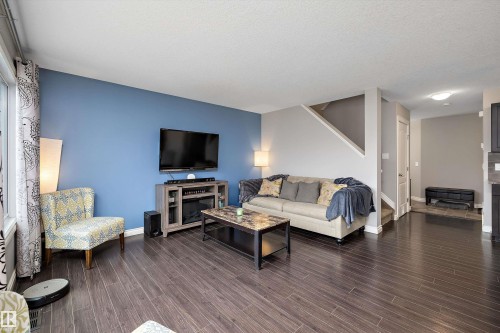 Spacious living area featuring wood-finish flooring, a contemporary accent wall, and an open staircase - 3922 Agar Court Sw, Edmonton, AB - Indoor Photo Showing Living Room