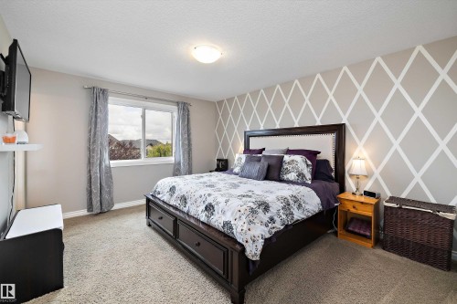 Carpeted room featuring a window, built-in ceiling light, and accent wall with a geometric pattern - 3922 Agar Court Sw, Edmonton, AB - Indoor Photo Showing Bedroom