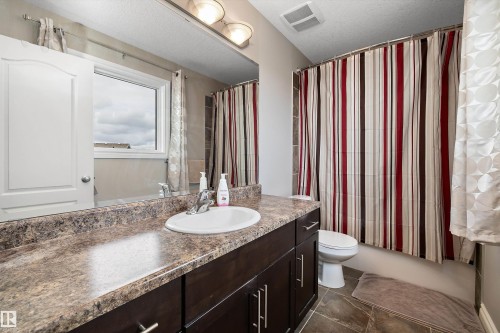 Bathroom featuring a vanity with a single basin sink, a large mirror, dark wood-finish cabinetry, patterned countertop, and tile flooring - 3922 Agar Court Sw, Edmonton, AB - Indoor Photo Showing Bathroom