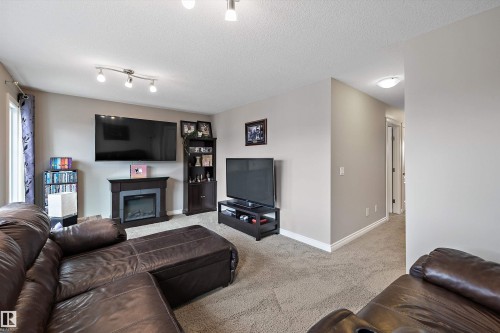 Electric fireplace with a dark wood-finish mantel and surround, track lighting, and neutral wall paint - 3922 Agar Court Sw, Edmonton, AB - Indoor Photo Showing Living Room With Fireplace