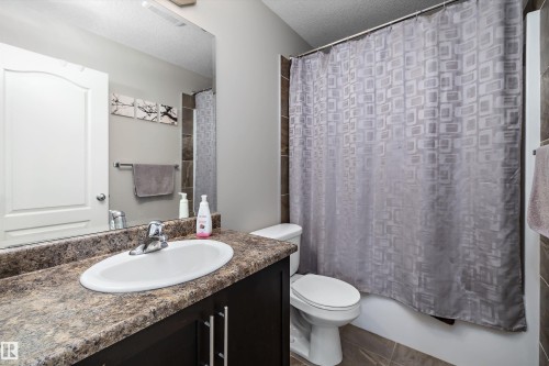 Bathroom featuring a vanity with a counter and an integrated sink, a built-in mirror, and a shower with tile surround - 3922 Agar Court Sw, Edmonton, AB - Indoor Photo Showing Bathroom