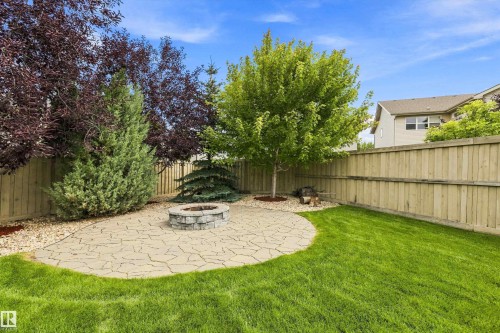 Expansive backyard featuring a stone paver patio, integrated fire pit, manicured lawn, and mature landscaping - 3922 Agar Court Sw, Edmonton, AB - Outdoor With Backyard