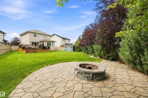 Expansive rear yard featuring a stone fire pit, irregular flagstone patio, and a spacious wooden deck with railings - 3922 Agar Court Sw, Edmonton, AB - Outdoor With Deck Patio Veranda With Backyard