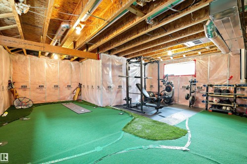 Finished basement featuring exposed wood-beam ceiling with recessed lighting, protective plastic wall coverings, synthetic turf flooring with custom white striping, and built-in storage shelving - 3922 Agar Court Sw, Edmonton, AB - Indoor Photo Showing Basement