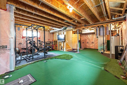 Exposed wood joist ceiling, green artificial turf flooring, built-in staircase, wall-mounted television, and overhead lighting - 3922 Agar Court Sw, Edmonton, AB - Indoor Photo Showing Basement
