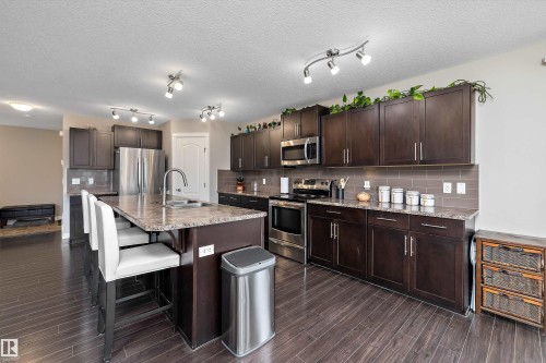 Kitchen featuring a large island with sink, dark wood-finish cabinetry, stainless steel appliances, and a tile backsplash - 3922 Agar Court Sw, Edmonton, AB - Indoor Photo Showing Kitchen With Double Sink With Upgraded Kitchen