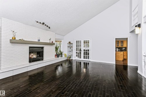 Spacious interior featuring a vaulted ceiling, dark wood-finish flooring, a white brick fireplace with a mantel, and double french doors - 6016 177 Street Nw, Edmonton, AB - Indoor With Fireplace
