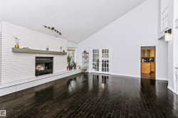 Spacious interior featuring a vaulted ceiling, dark wood-finish flooring, a white brick fireplace with a mantel, and double french doors - 