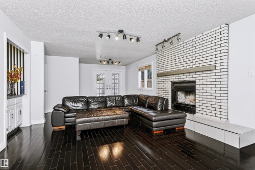 Dark wood-finish flooring, white painted brick fireplace with hearth, built-in white cabinetry, track lighting fixtures, and white French doors - 6016 177 Street Nw, Edmonton, AB - Indoor Photo Showing Living Room With Fireplace