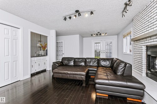 Dark wood-finish flooring, white painted brick fireplace with a mantel, built-in cabinetry, French doors, and track lighting fixtures - 6016 177 Street Nw, Edmonton, AB - Indoor Photo Showing Living Room With Fireplace