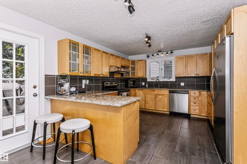 Kitchen featuring wood cabinetry, stainless steel appliances, a black tile backsplash, and a granite-style countertop on the island - 6016 177 Street Nw, Edmonton, AB - Indoor Photo Showing Kitchen With Stainless Steel Kitchen