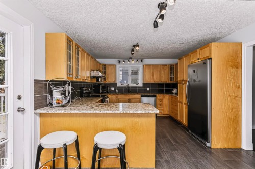 Kitchen with extensive wood-finish cabinetry, a built-in breakfast bar, and dark tiled backsplash - 6016 177 Street Nw, Edmonton, AB - Indoor Photo Showing Kitchen