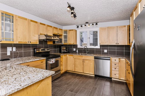 Kitchen featuring wood cabinetry, granite countertops, tile backsplash, and stainless steel appliances - 6016 177 Street Nw, Edmonton, AB - Indoor Photo Showing Kitchen With Stainless Steel Kitchen