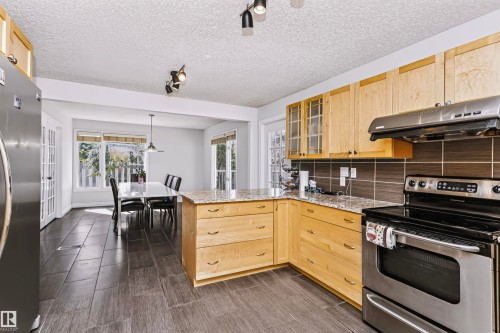 Kitchen featuring granite-look countertops, light wood cabinetry, stainless steel appliances, and a tile backsplash - 6016 177 Street Nw, Edmonton, AB - Indoor Photo Showing Kitchen