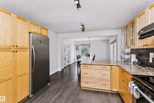 Kitchen featuring wood-finish cabinetry, granite countertops, tile flooring, and a stainless steel refrigerator - 6016 177 Street Nw, Edmonton, AB - Indoor Photo Showing Kitchen