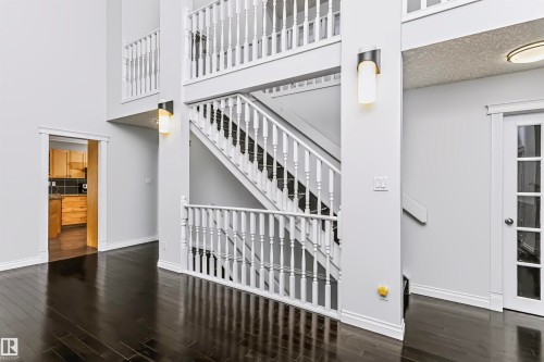 Multi-level interior featuring dark wood-finish flooring, a two-story staircase with white balusters, white trim, and wall-mounted sconces - 6016 177 Street Nw, Edmonton, AB - Indoor Photo Showing Other Room