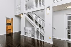 Multi-level interior featuring dark wood-finish flooring, a two-story staircase with white balusters, white trim, and wall-mounted sconces - 