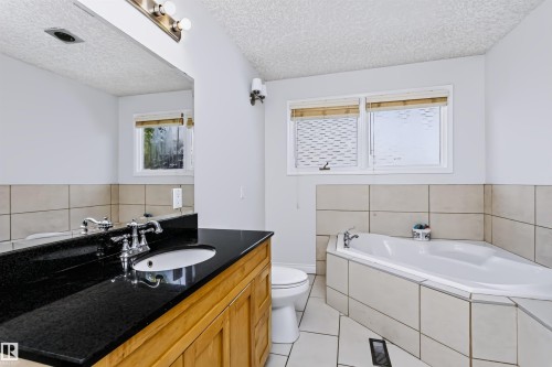 Wood-finish vanity with a dark countertop and integrated sink - 6016 177 Street Nw, Edmonton, AB - Indoor Photo Showing Bathroom