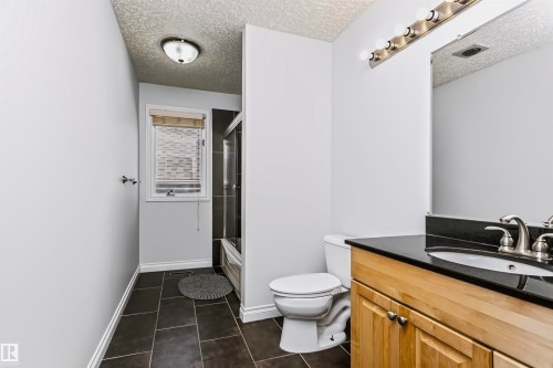 Bathroom featuring a wood-finish vanity with a dark countertop, an integrated sink, and a framed mirror - 6016 177 Street Nw, Edmonton, AB - Indoor Photo Showing Bathroom