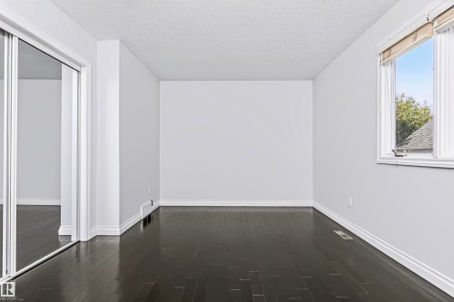 Dark wood-finish flooring, white trim, and a window with a white frame - 6016 177 Street Nw, Edmonton, AB - Indoor Photo Showing Other Room
