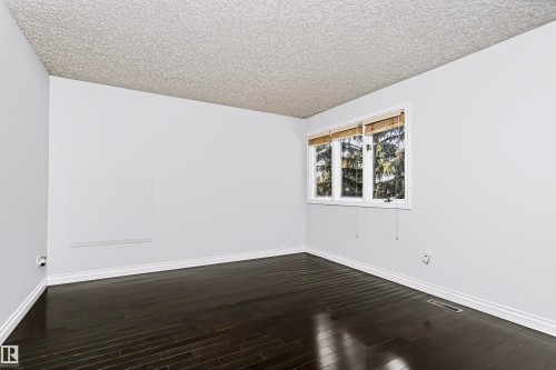 Dark wood-finish flooring with white baseboards, a white wall finish, and a textured ceiling - 6016 177 Street Nw, Edmonton, AB - Indoor Photo Showing Other Room