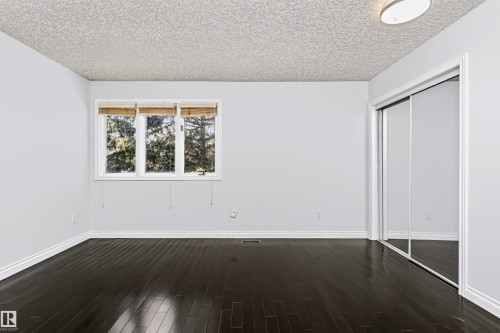 Dark wood-finish flooring, white walls, triple window with natural light, mirrored sliding closet doors, and a flush-mount ceiling light - 6016 177 Street Nw, Edmonton, AB - Indoor Photo Showing Other Room