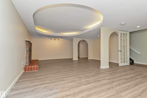 Expansive room featuring wood-finish flooring, a brick fireplace with a tile hearth, and an arched doorway - 6016 177 Street Nw, Edmonton, AB - Indoor