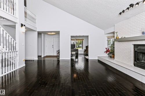 Vaulted ceilings, dark wood-finish flooring, white brick fireplace with a mantel, and a multi-level staircase with white balusters - 6016 177 Street Nw, Edmonton, AB - Indoor With Fireplace