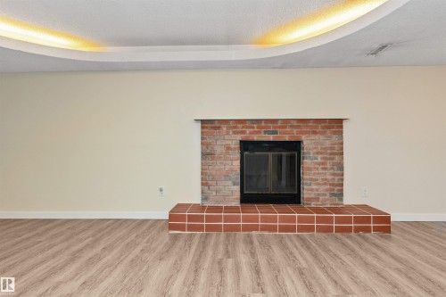 Recessed lighting in a curved ceiling feature, brick fireplace with a tile hearth, and wood-finish flooring - 6016 177 Street Nw, Edmonton, AB - Indoor With Fireplace