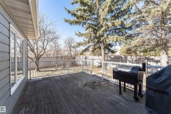 Expansive wooden deck with a white railing system, featuring a large window, and bordered by a privacy fence and mature trees - 