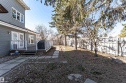 Spacious backyard featuring a wooden deck with white railings, a concrete paver pathway, mature trees, and a perimeter fence - 