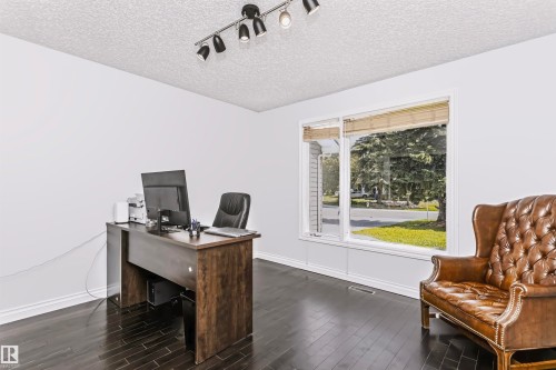 Dark wood-finish flooring with white baseboards, bright white walls, and a large window with natural light - 6016 177 Street Nw, Edmonton, AB - Indoor Photo Showing Office