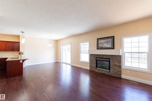 Rich wood-finish flooring, stone-clad fireplace with mantel, sliding glass door, kitchen island with granite countertop, and pendant lighting - 1419 Chahley Place Nw, Edmonton, AB - Indoor Photo Showing Living Room With Fireplace