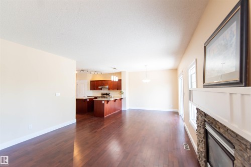 Hardwood-finish flooring, stone-clad fireplace with mantel, recessed lighting, and kitchen island with pendant lighting - 1419 Chahley Place Nw, Edmonton, AB - Indoor Photo Showing Other Room