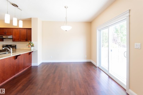 Hardwood flooring throughout, kitchen with wood cabinetry and light-toned countertops, recessed lighting, and sliding glass door - 1419 Chahley Place Nw, Edmonton, AB - Indoor Photo Showing Kitchen With Double Sink