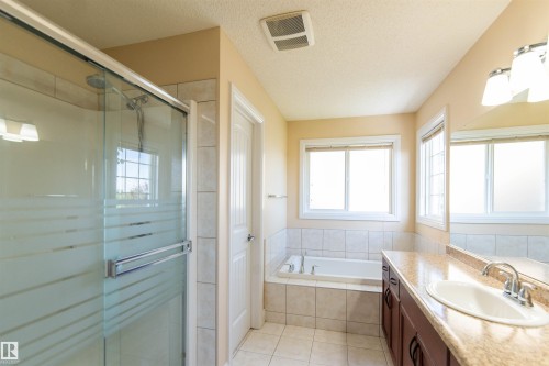 Walk-in shower with clear and frosted glass enclosure, deep soaking tub, dual windows, vanity with integrated sink, and large wall-mounted mirror - 1419 Chahley Place Nw, Edmonton, AB - Indoor Photo Showing Bathroom