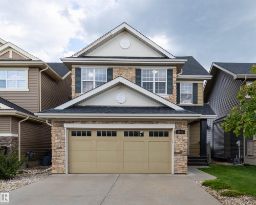 Two-story exterior featuring stone and siding finishes, a two-car garage with transom windows, a concrete driveway, and a covered entry - 1419 Chahley Place Nw, Edmonton, AB - Outdoor With Facade