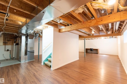 Spacious lower level featuring wood-finish flooring, exposed ceiling joists, and a partial staircase with carpeted treads - 1419 Chahley Place Nw, Edmonton, AB - Indoor Photo Showing Basement