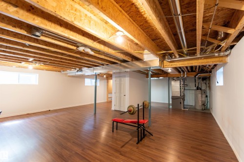 Expansive lower level featuring wood-finish flooring, exposed ceiling joists, and white painted walls - 1419 Chahley Place Nw, Edmonton, AB - Indoor Photo Showing Basement