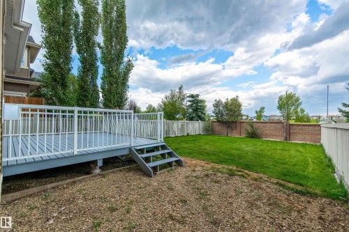 Expansive backyard featuring a manicured lawn, a raised wood deck with white railings, and a partial brick privacy fence - 1419 Chahley Place Nw, Edmonton, AB - Outdoor