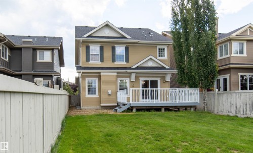 Expansive backyard featuring a manicured lawn, a raised wood-finish deck with white railings, and mature trees - 1419 Chahley Place Nw, Edmonton, AB - Outdoor With Deck Patio Veranda